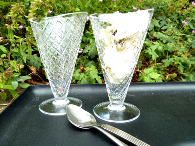 Tutti frutti ice cream in sundae dishes served outside on a table with bushes behind the table.