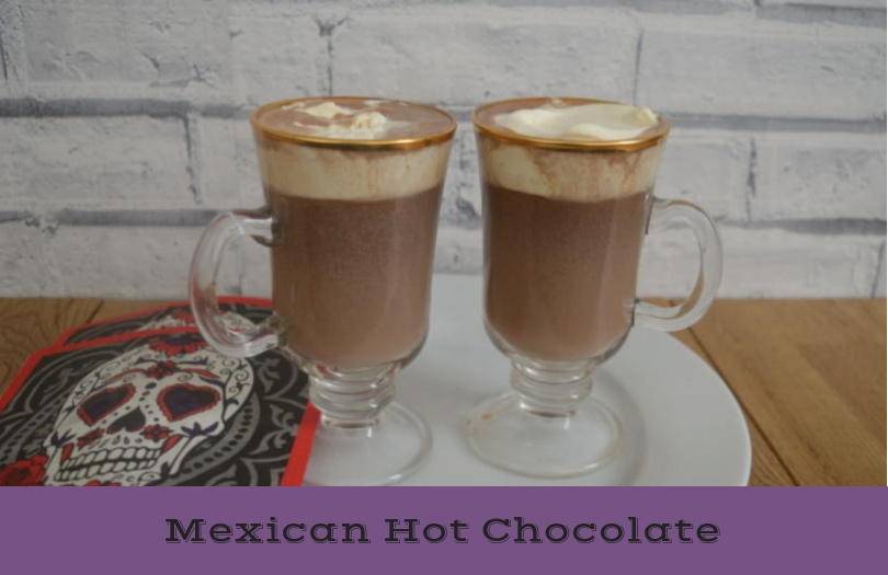 Two tall glasses of mexican hot chocolate with cream topping on a table