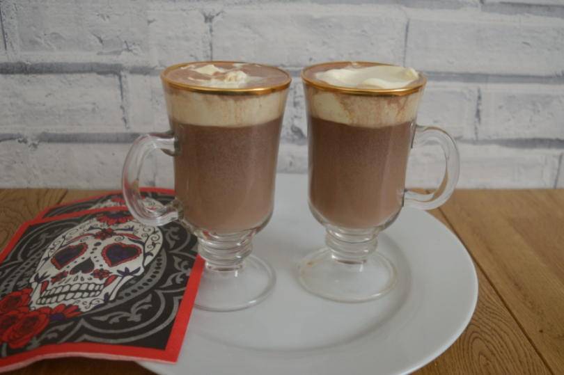 two glasses of Mexican hot chocolate with cream on top on a plate