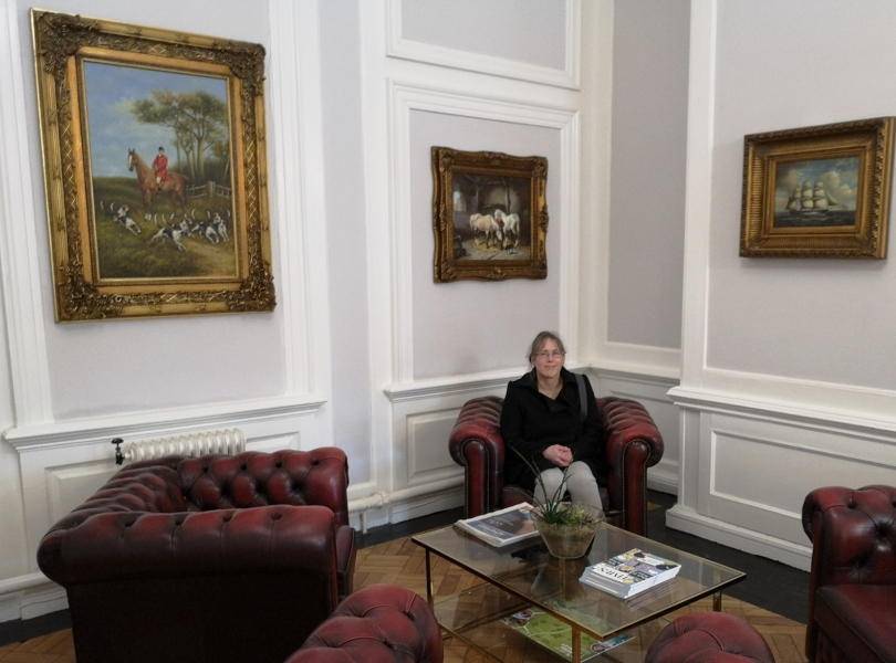 A lady sitting on a seat in Beamish hall hotel entrance with paintings on the wall