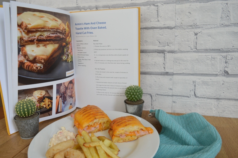 Ham and cheese toastie on a plate with a picture from the cookbook behind