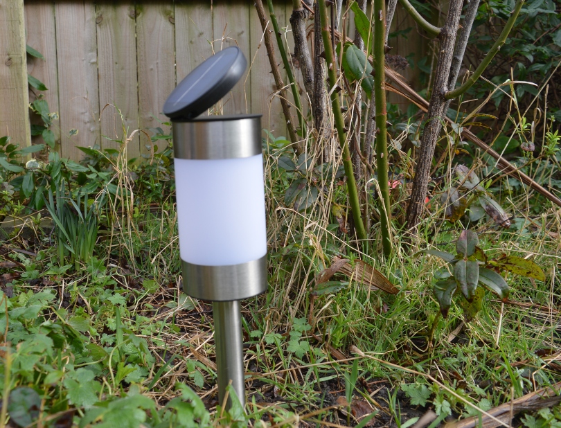 A stake solar light with the panel tilted to catch the light in the garden