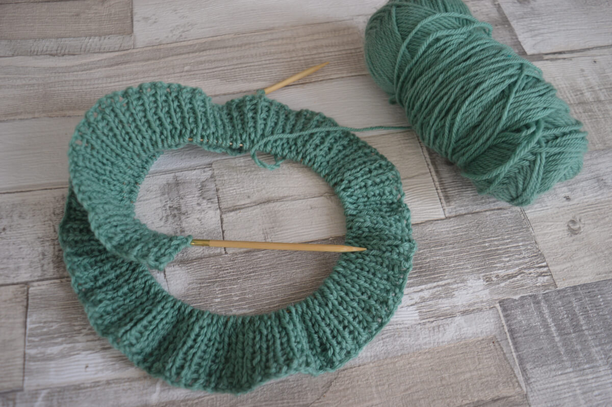 Rows of rib stitch knitting in green wool with the ball of wool beside