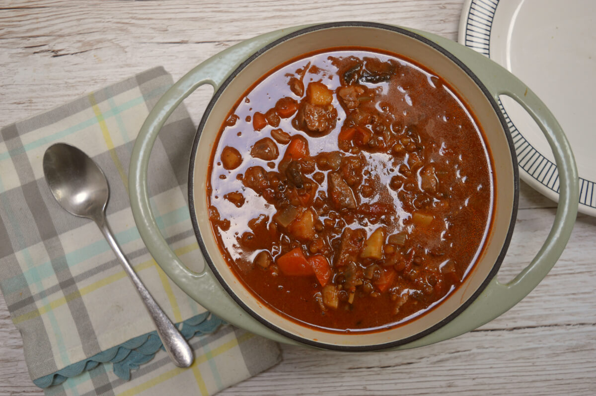 lamb and lentil stew in a casserole dish with a green napkin and spoon beside it on a table