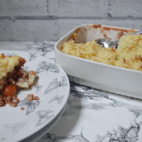 Slice of homemade cottage pie with minced beef and carrot filling topped with golden mashed potato