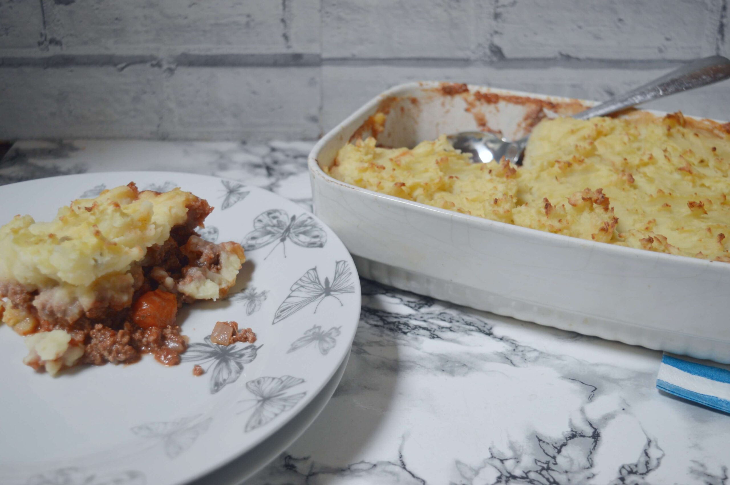 Slice of homemade cottage pie with minced beef and carrot filling topped with golden mashed potato