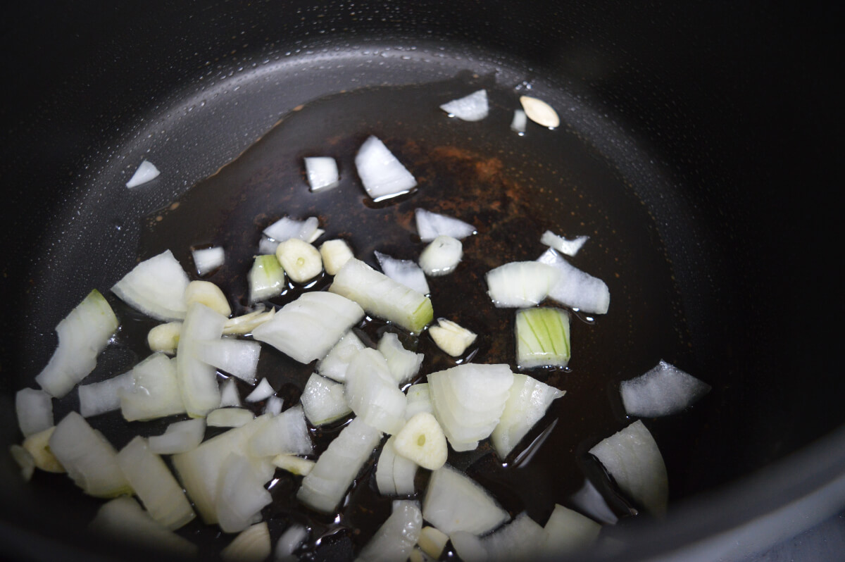Chopped onion and sliced garlic cooking in oil in a saucepan, the first step in making pumpkin soup.