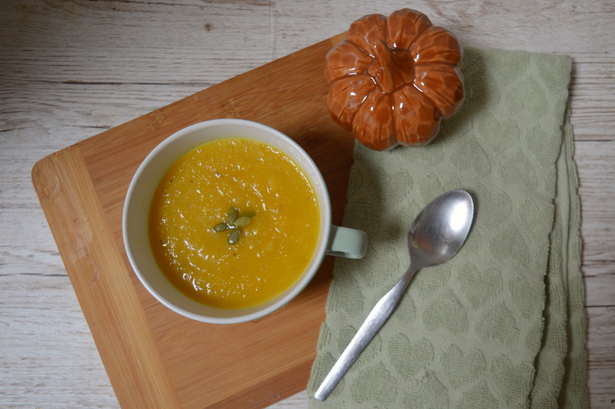 Overhead view of homemade pumpkin soup in a pale green cup, topped with four pumpkin seeds arranged in a flower shape.