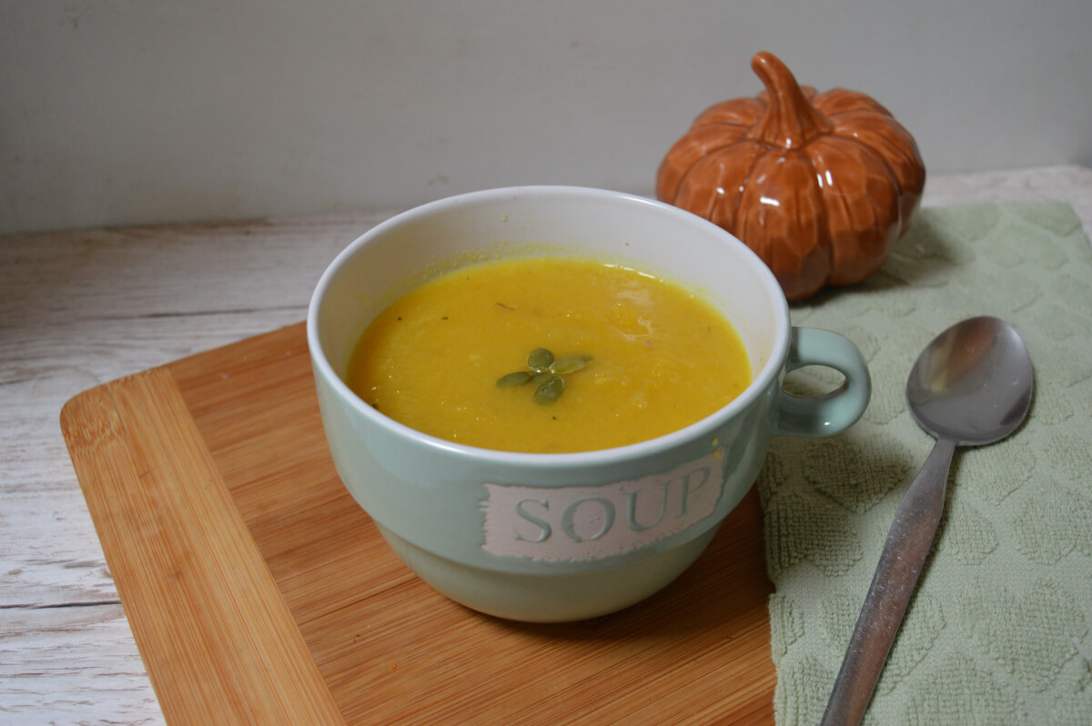 Warming spiced pumpkin soup in a pale green soup cup, garnished with pumpkin seeds beside an autumn pumpkin decoration.