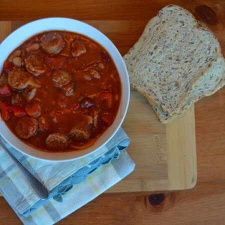 sausage and bean soup in a bowl on a table with a slice of bread beside it
