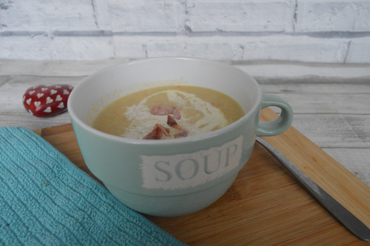 A green bowl with soup written on the side containing neep and tattie soup topped with bacon. It is on a 