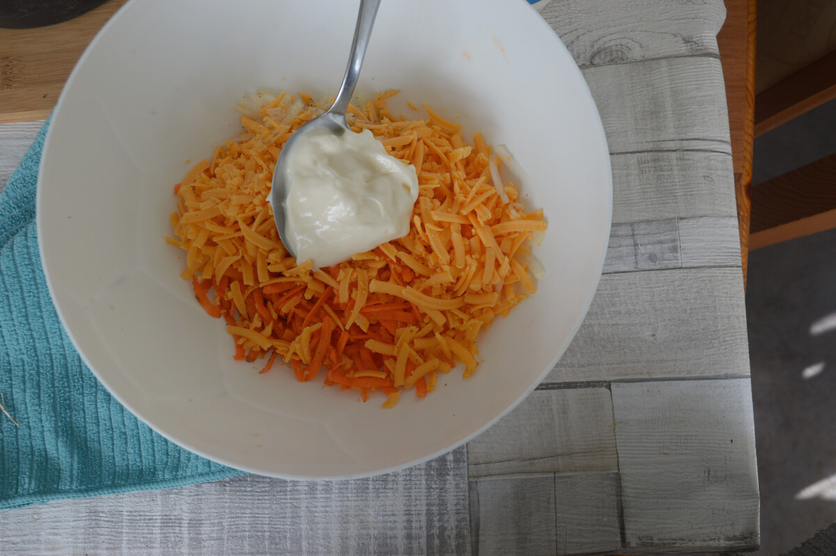 Mayonnaise being added to grated cheese, carrots and onions in a bowl 