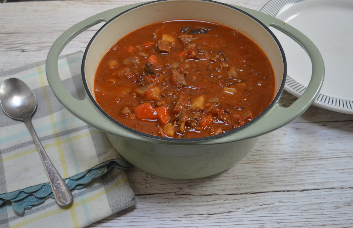 Lamb and lentil stew in a casserole dish on a table. There is a spoon and plate beside the dish.