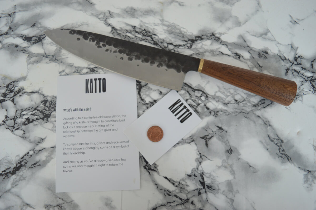 A chef knife on a marble surface with a penny on card beside it and information about why a penny is sent with a knife