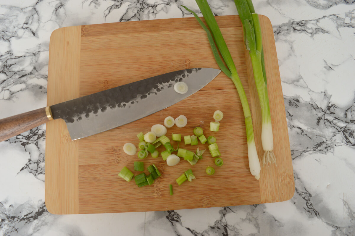 A knife on a chopping board with chopped up spring onions