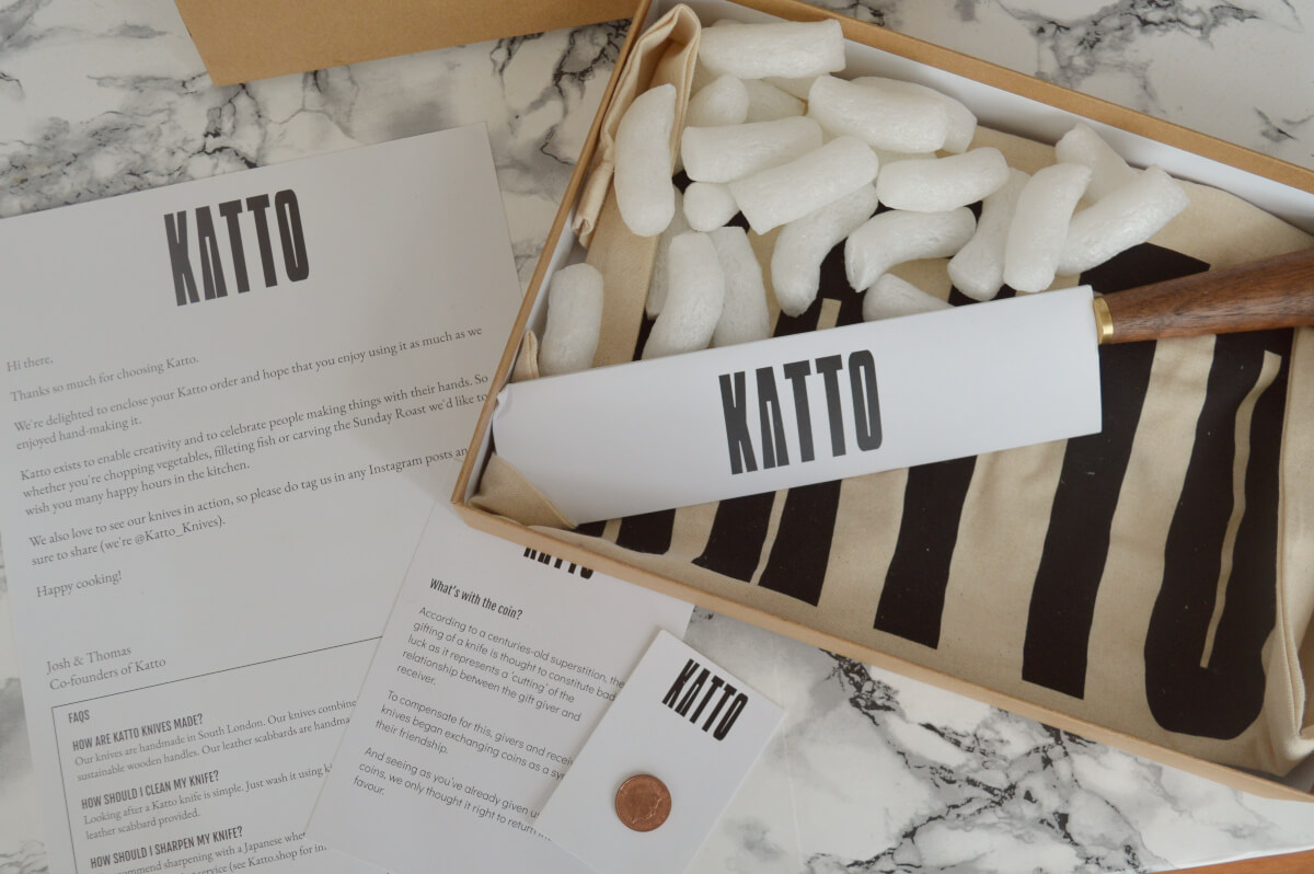 A cardboad box containing the Katto chef knife with a scabbard, leaflets that come with it and a tote bag.