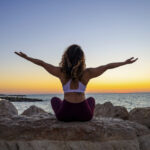 Woman sitting on stone doing yoga looking at sunset