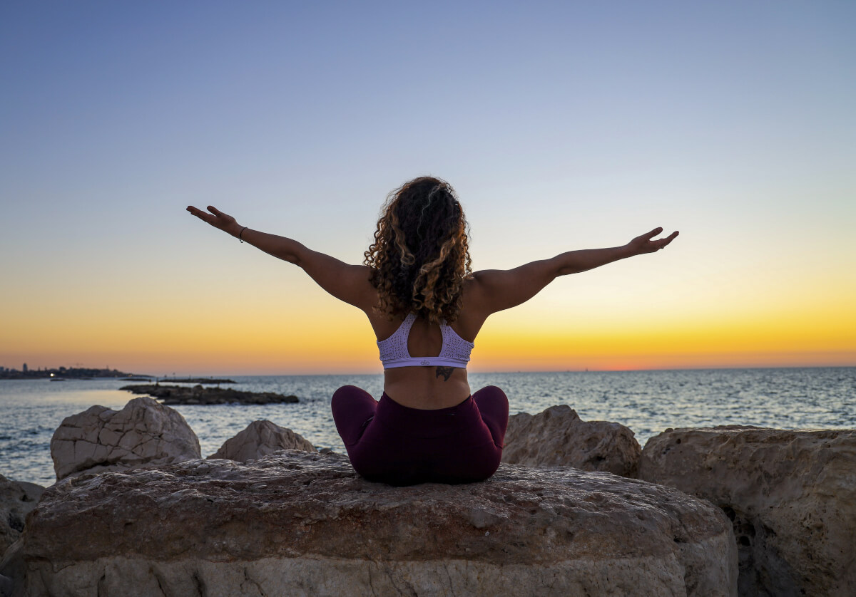 Woman sitting on stone doing yoga looking at sunset