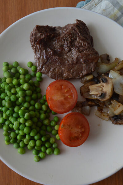 Steak on a white plate with tomatoes, peas and fried onions
