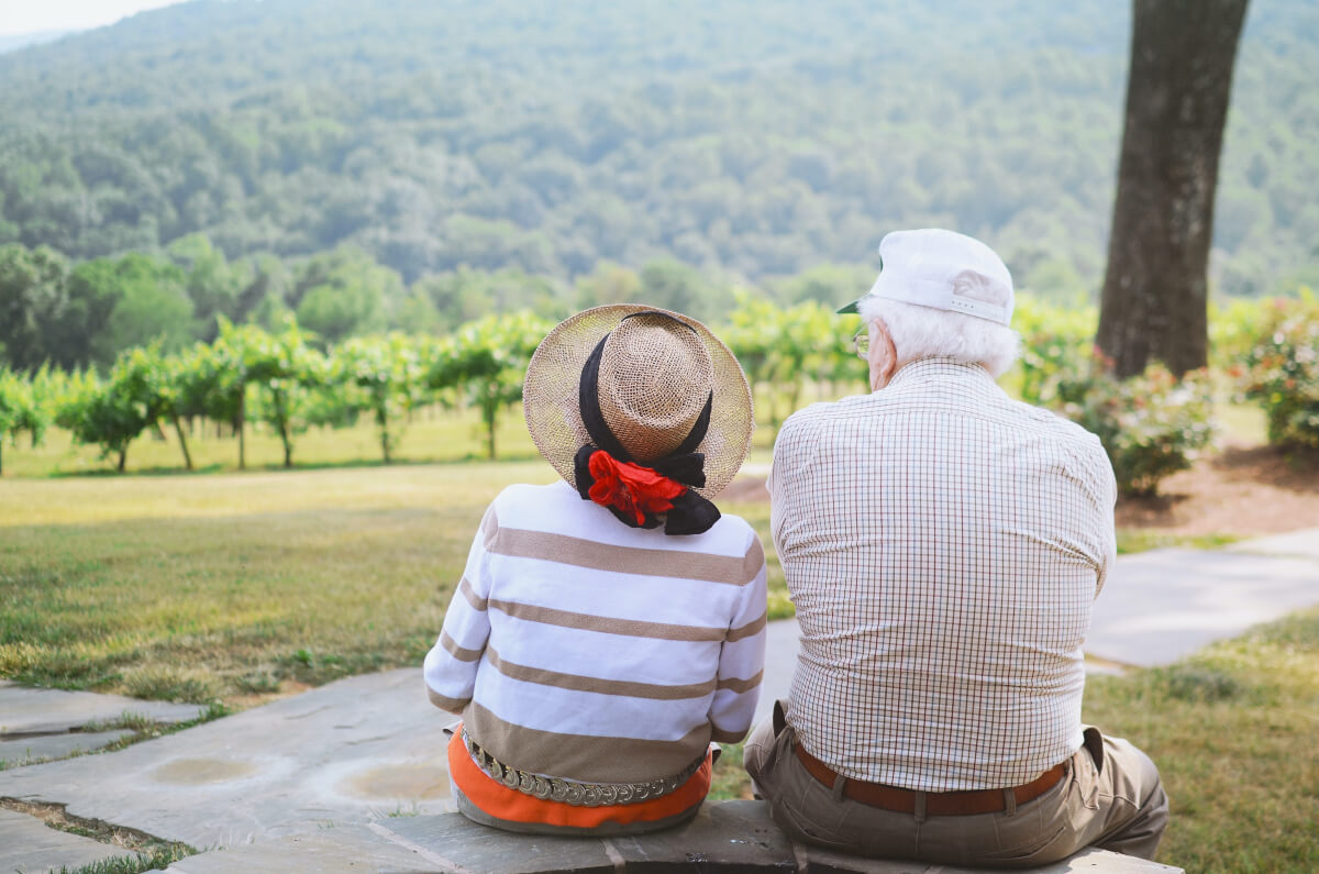 An elderly couple sitting on a step looking across a vineyard