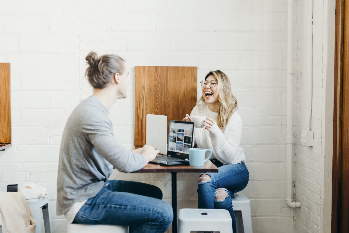 Couple sitting on a table opposite each other with coffee and laptops
