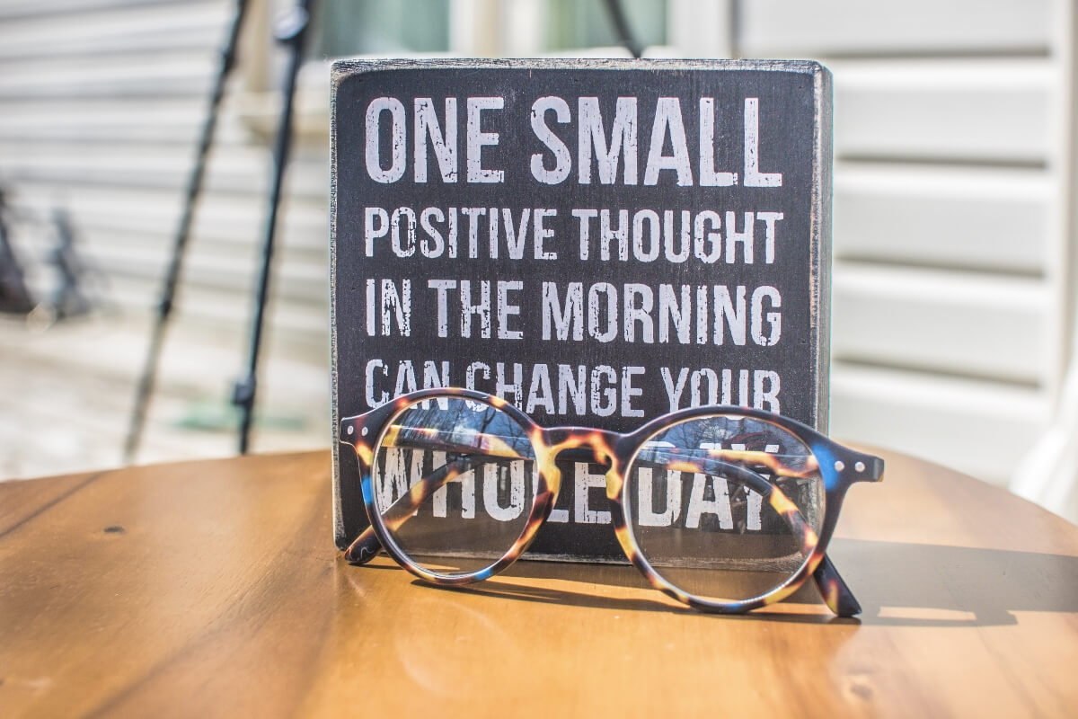 A sign with a positive message on a table with eyeglasses in front of it