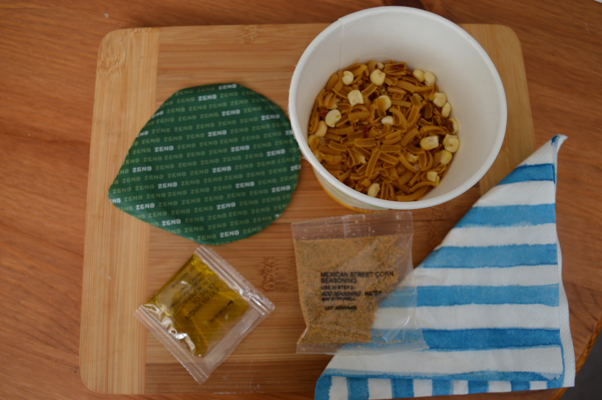 The contents of a pasta agile bowl, the opened bowl, flavour sachet and olive oil on a table