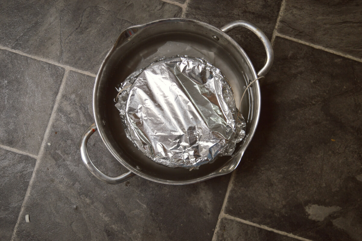 A pudding basin topped with silver foil in a large pan of water