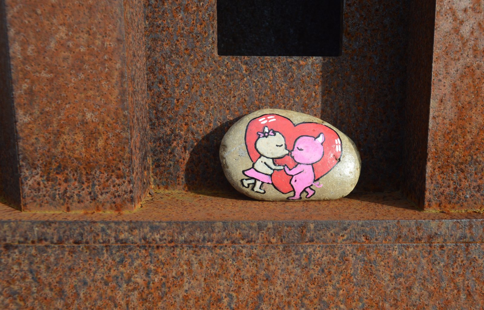 A small stone with a heart and two figures kissing painted on it