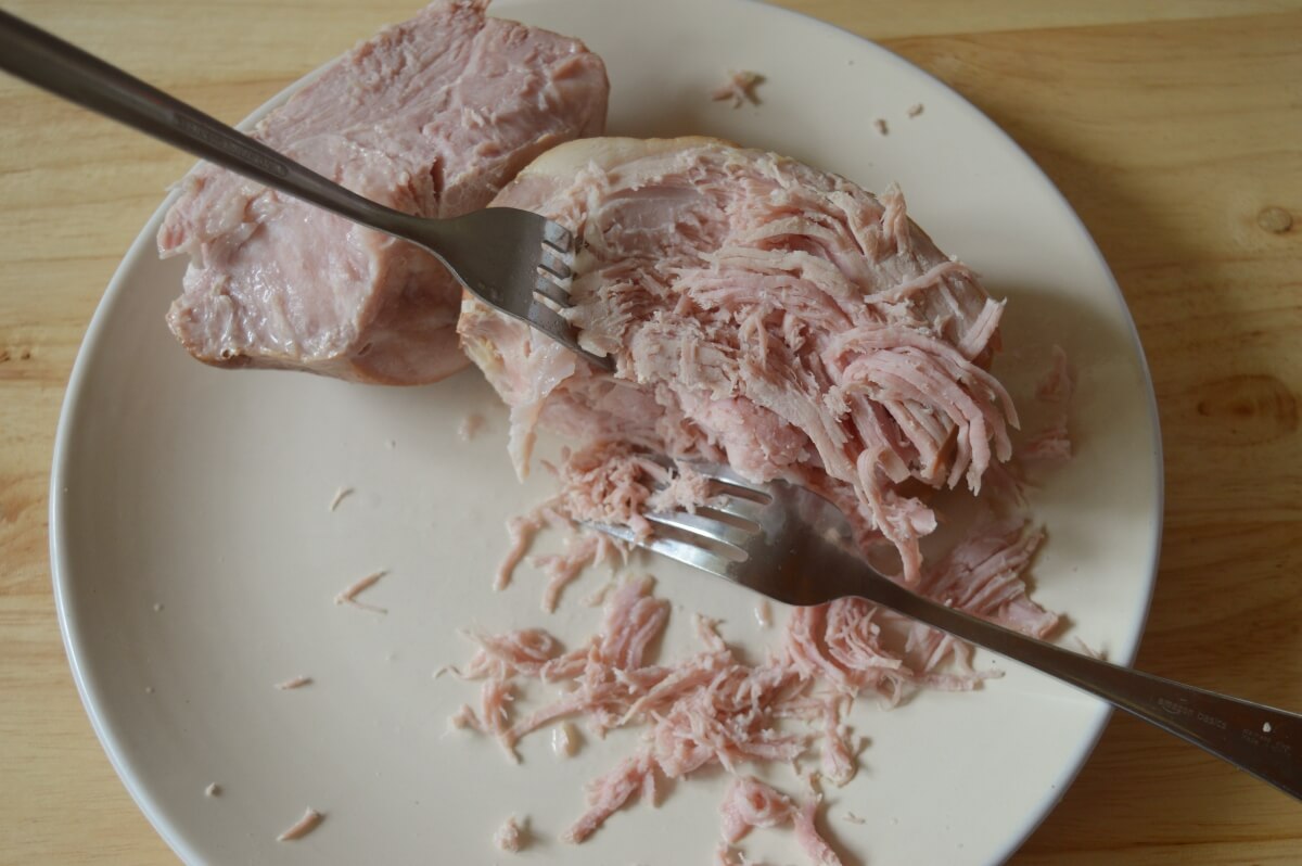 Shredding the cooked ham into bite-sized pieces.